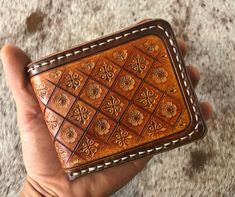 a hand holding a brown leather wallet on top of a carpeted floor with white stitching