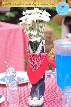 a cowboy boot vase filled with flowers on top of a red and white checkered table cloth