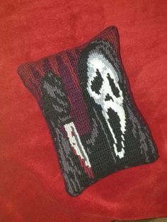 a knitted pillow with a skull design on it sitting on a red couch cushion