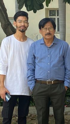 two men standing next to each other in front of a tree