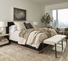 a bedroom with a large bed, chair and ottoman in front of a window that overlooks the city