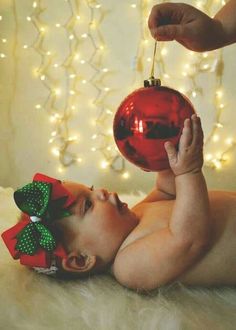 a baby laying on its back with a christmas ornament hanging from it's head