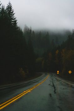 an empty road with trees and fog in the background