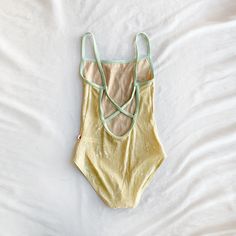 a yellow and green one piece swimsuit laying on top of a white sheeted bed