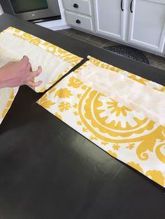 a person is cutting fabric on top of a table with yellow and white designs in the background