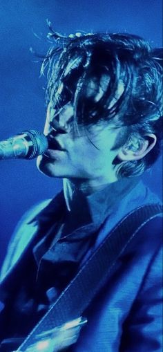 a man with dreadlocks on his face singing into a microphone while holding a guitar