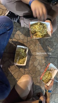 three people sitting on the ground with boxes of food in front of them and one person holding a cell phone