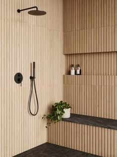 a bathroom with wood paneling and black shower faucet next to a plant