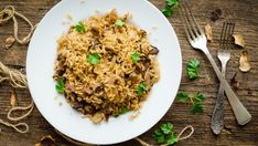 a white plate topped with rice and mushrooms next to silverware on a wooden table