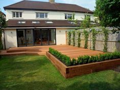 a wooden deck in front of a house with plants growing on the sides and around it