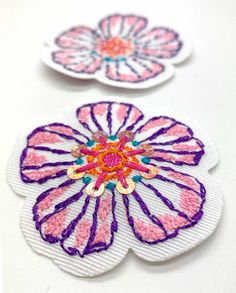 two flower shaped patches sitting on top of a white table next to eachother