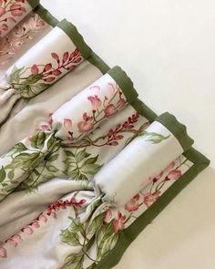 three folded towels with pink flowers on them and green trim around the edges, sitting on a white surface