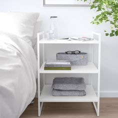 a white shelf next to a bed with books and glasses on it, along with other items