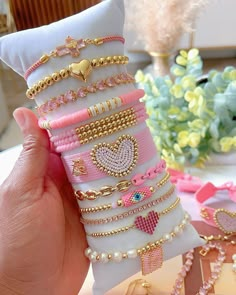 a hand holding a stack of bracelets on top of a white pillow next to a vase