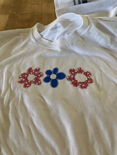 two t - shirts with red, white and blue flowers on them sitting on a wooden floor