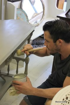 a man sitting on the floor with a paint can and brush in his mouth while painting a table