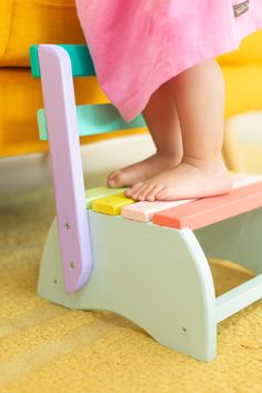 a child's feet on a colorful wooden toy step stool in front of a yellow chair