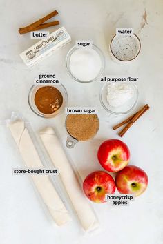 ingredients to make apple pie laid out on a white counter top with apples, cinnamon sticks, flour, sugar and other items