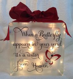 a lighted glass block with a red bow on it's side that says, when a butterfly appears in your yard, it is a visitor from heaven