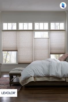 a bed sitting under two windows in a bedroom next to a window with blind shades