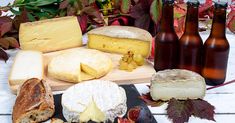 several different types of cheeses and wine on a wooden table with autumn leaves around them