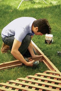 a man working on some kind of wooden structure in the grass with tools and supplies