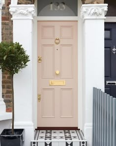 a pink front door with black and white tiles on the floor next to a potted plant