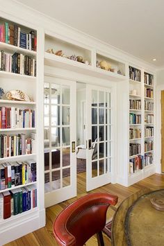 a living room filled with lots of books on top of white bookcases next to a table