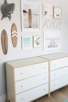 a white dresser sitting next to a wall filled with pictures and surfboards on top of it