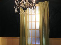 a chandelier hanging from the ceiling in front of a window with green curtains