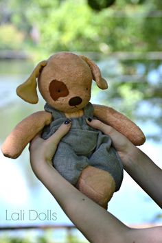 a person holding a teddy bear in their hand with trees and water in the background