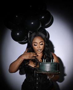 a woman holding a cake with candles on it in front of some black balloons,