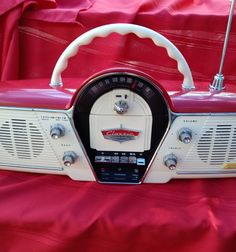 an old fashioned radio sitting on top of a red cloth covered tablecloth with a steering wheel