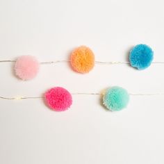 four pom - poms hanging on a string against a white wall, one is multicolored