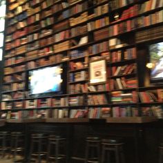 a large book shelf filled with lots of books next to bar stools and tables