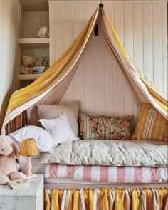 a bed with a canopy over it next to a pink teddy bear on a table