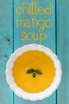 a white bowl filled with yellow soup on top of a blue wooden table and the words chilled mango soup above it