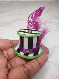 a hand holding a small hat with a purple and green feather on it's top