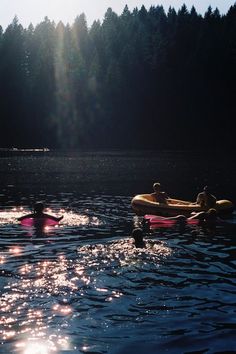 three people are floating on inflatable rafts across the water with trees in the background