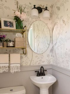 a white sink sitting under a bathroom mirror next to a shelf with flowers on it