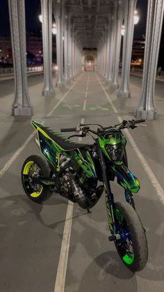 a green and black dirt bike parked in a parking lot next to tall pillars at night