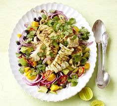 a white plate topped with chicken and veggies next to a silver spoon on top of a table