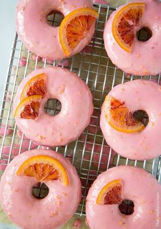 donuts with pink icing and orange slices on a cooling rack, ready to be eaten