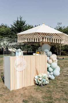 an outdoor bar set up with balloons, flowers and other decorations on the grass in front of a white tent