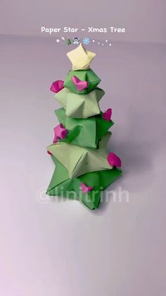 an origami christmas tree with pink and green stars on it's top