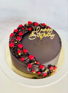 a chocolate birthday cake decorated with red and yellow flowers on a white plate that says happy birthday