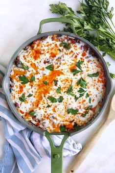 a casserole with cheese and herbs in a green pan on a white table