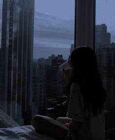 a woman sitting on top of a bed next to a window in a tall building