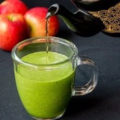 a glass cup filled with green liquid next to apples