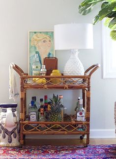 a wicker bar cart with liquor bottles and pineapples on it in a living room